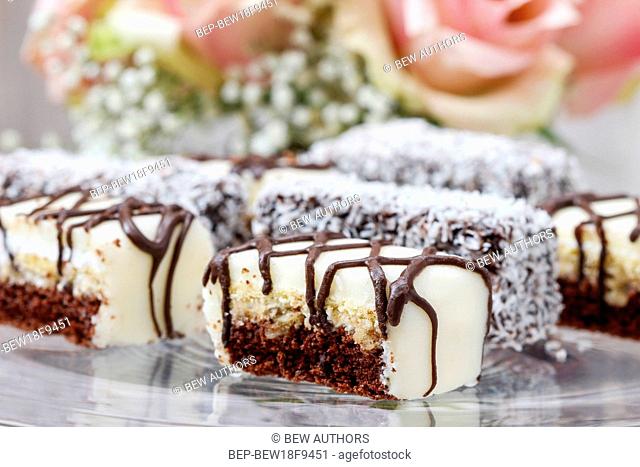 Chocolate and marzipan cakes on glass cake stand. Bouquet of pink roses in the background