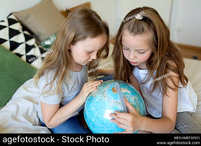 Two sisters sitting together on bed looking at globe