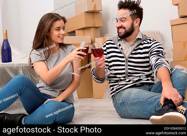 Young couple celebrating apartment purchase. Smiling man and woman sitting on the floor with wineglasses in their hands