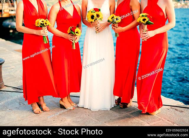 Bridesmaids in red dresses, in hands bouquets of sunflowers. Wedding on the sea, in Montenegro