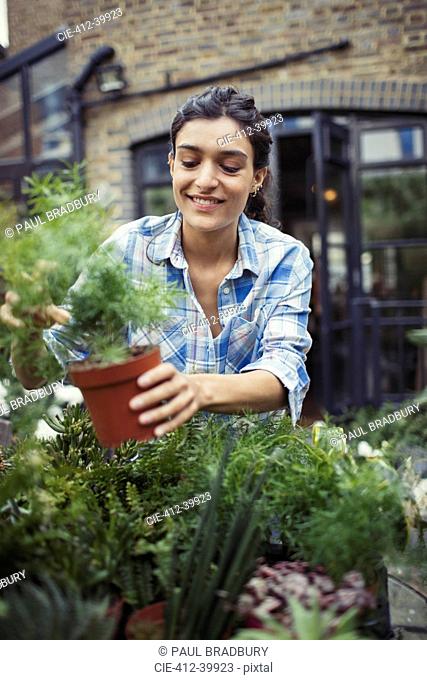 Young woman gardening, holding potted plant on patio