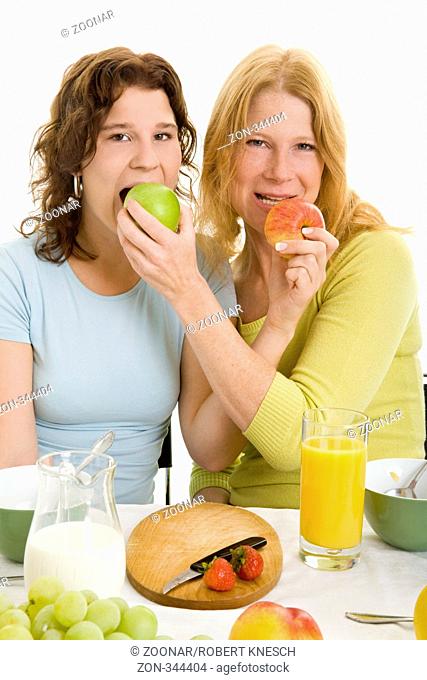 Mutter und Tochter am Frühstückstisch beißen gleichzeitig in zwei Äpfel