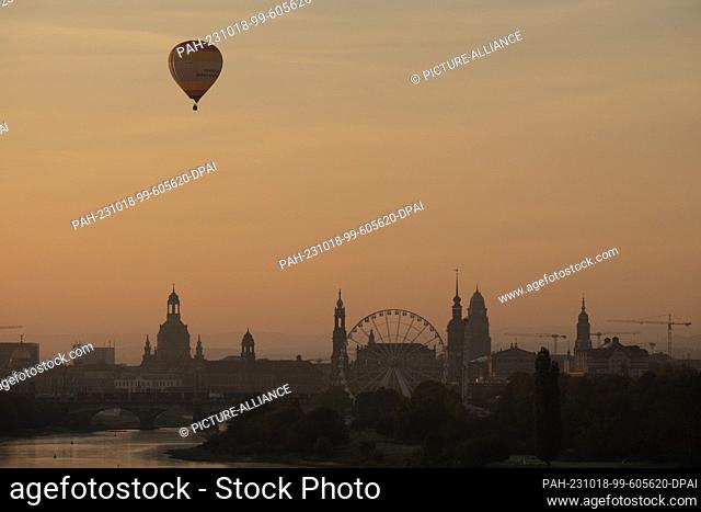 18 October 2023, Saxony, Dresden: A hot air balloon rides over the backdrop of the old town at sunrise. Photo: Sebastian Kahnert/dpa