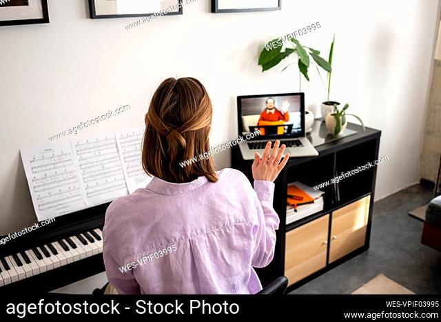 Mid adult woman waving during video call through laptop at home