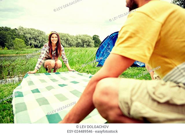 camping, travel, tourism, hike and people concept - happy couple laying picnic blanket at campsite