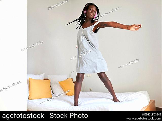 Carefree woman with arms outstretched standing on bed at home
