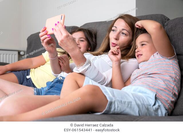 Happy mother with her kids are making a selfie or video call to father or relatives in a sofa. Concept of technology, new generation, family, connection