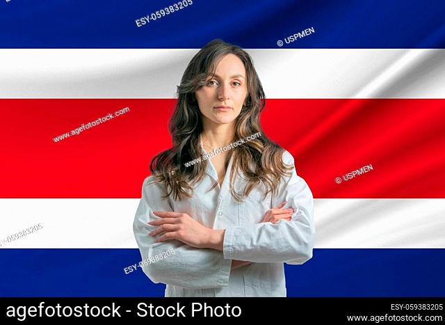 Medicine in Costa Rica Happy beautiful female doctor in medical coat standing with crossed arms against the background of the flag of Costa Rica