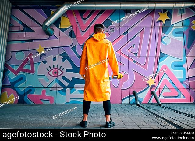 Back view of graffiti painter looking to the wall with his paintings. Street art concept