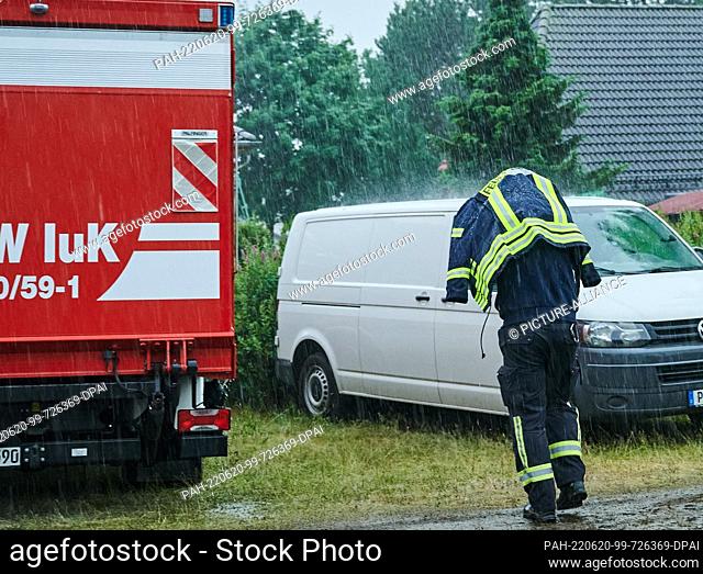 20 June 2022, Brandenburg, Treuenbrietzen: A firefighter protects himself from the heavy rain with his operational jacket while walking on the staging area near...