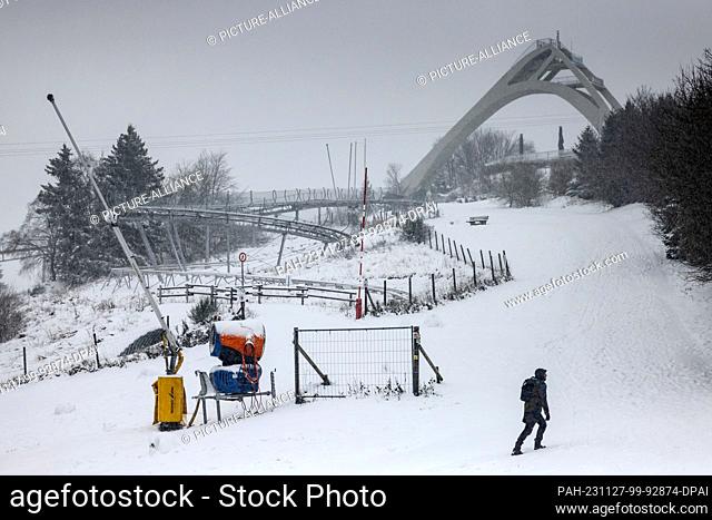 27 November 2023, North Rhine-Westphalia, Winterberg: A man walks in front of the ski jump in Winterberg. The cold and wet weather continues in North...