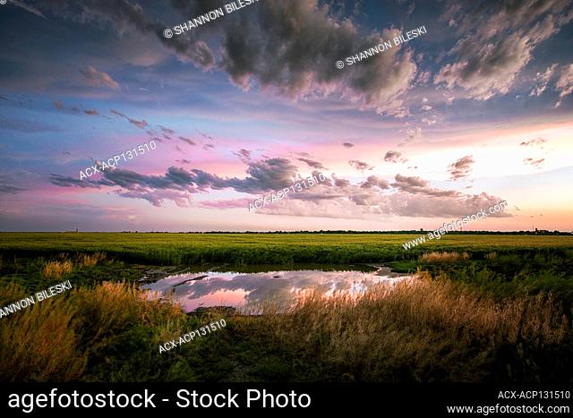 Sunset over a pond with a perfect reflection as a storm passes near Dodge City Kansas United States