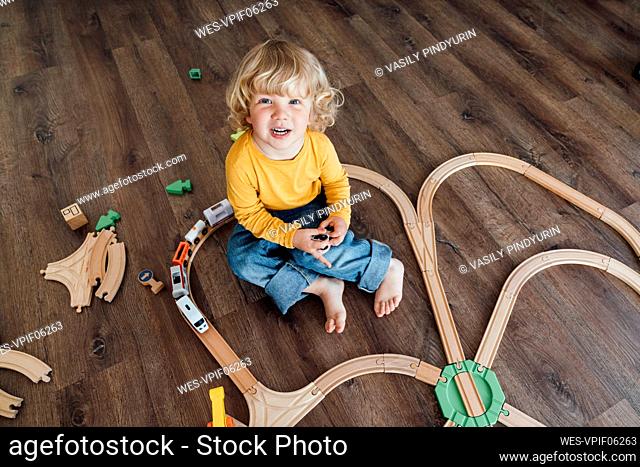 Happy boy with blond hair playing with toy train set at home