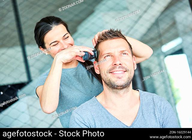 Mann bekommt von Frau als Friseur einen Haarschnitt mit der Haarschneidemaschine
