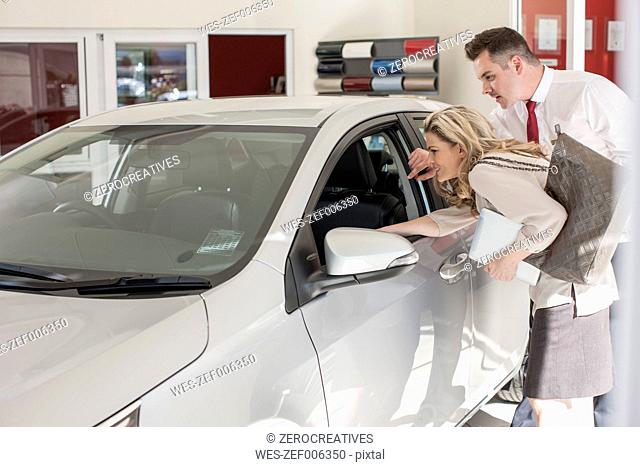Car dealer showing new car to woman in showroom