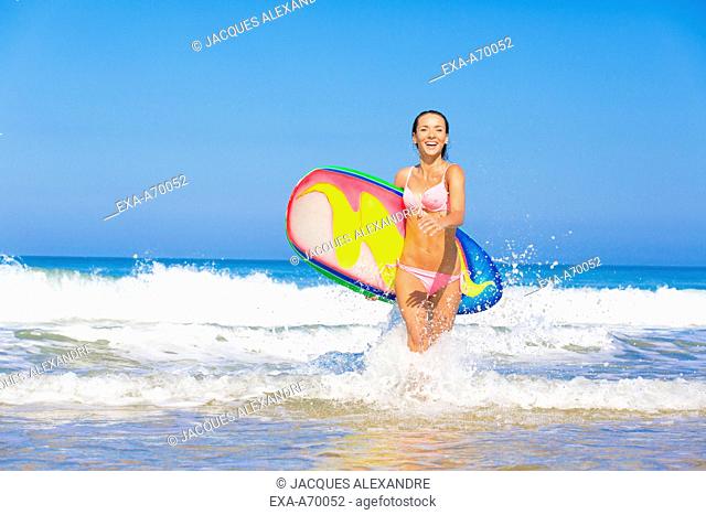 woman runs at beach with surfboard