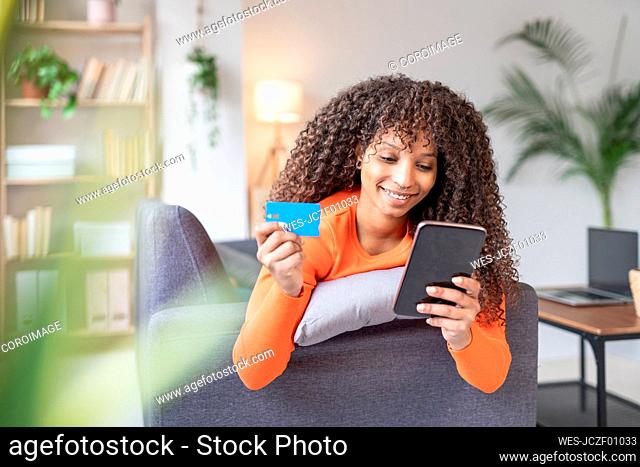 Smiling woman holding credit card using mobile phone at home