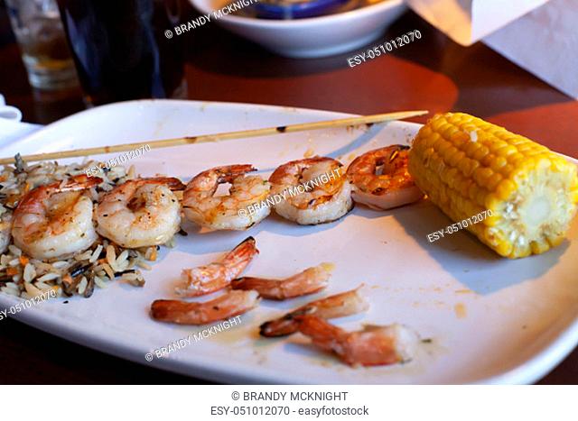 Grilled shrimp on a skewer plated with wild rice and corn on the cob