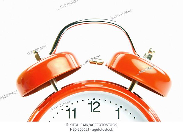 An old fahion analogue alarm clock set against a white background