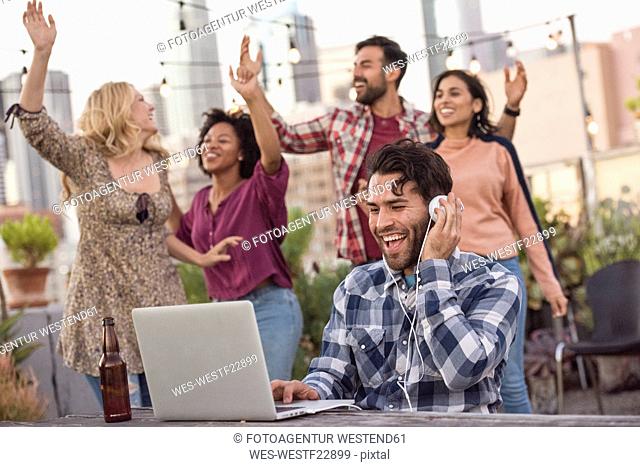 People dancing at rooftop party, with DJ using laptop