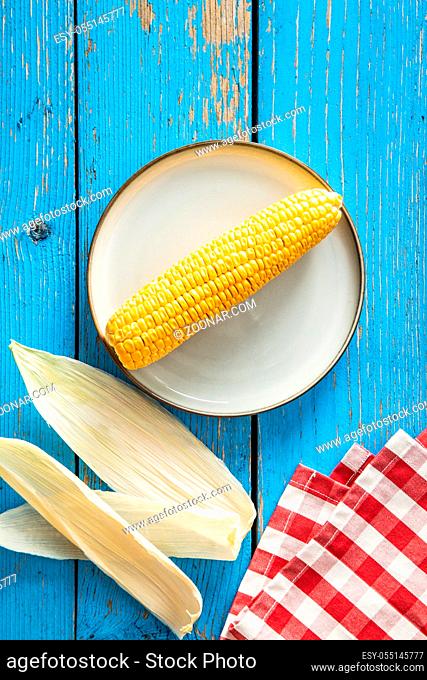 Uncooked corn cob on plate on blue wooden table. Top view