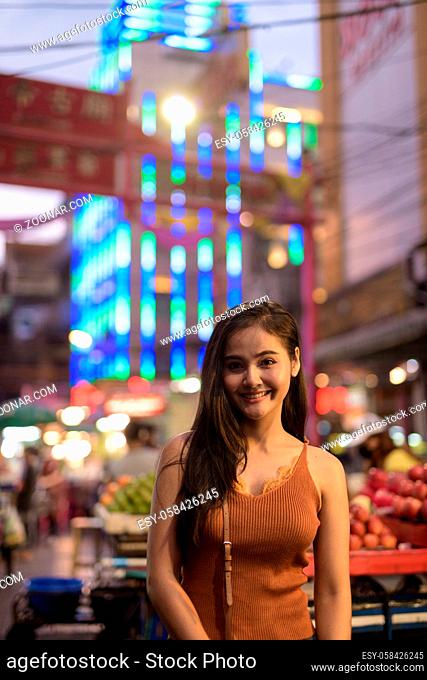 Portrait of young beautiful Asian tourist woman exploring Chinatown in Bangkok city at night