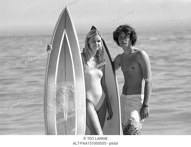 Couple holding surfboards, looking into camera, b&w