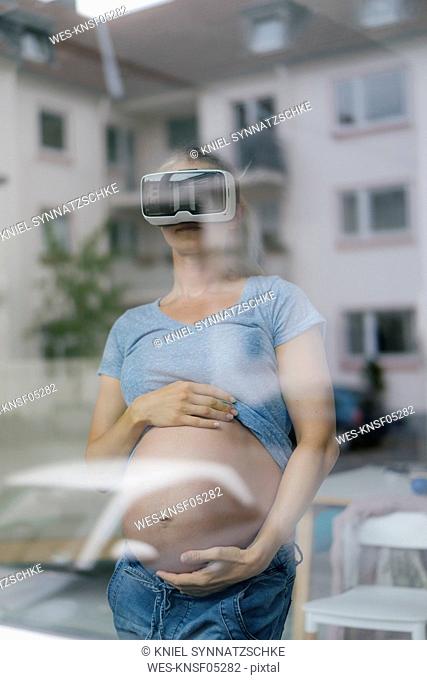 Pregnant woman wearing VR glasses behind windowpane