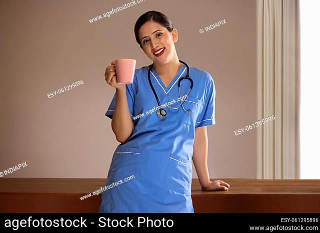 Portrait of a cheerful nurse standing with a cup of coffee in the hospital canteen