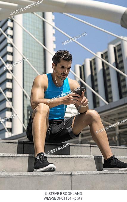 Runner wearing earphones, checking messages on his smartphone