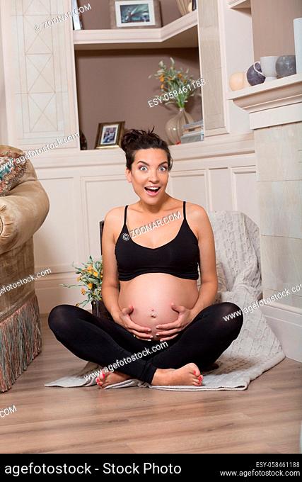 Pregnant lady meditating and touching her big belly in vintage interior while sitting on floor. Happy brunette lady smiling