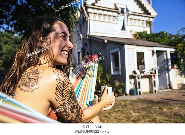 Happy young woman with tattoo in hammock