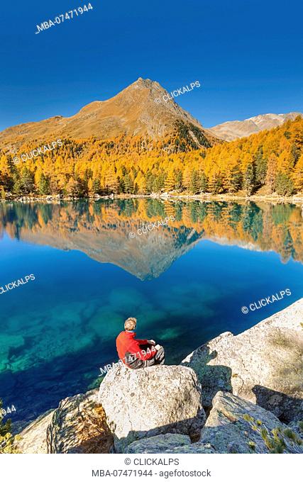 Hiker take a break to admire lake Saoseo in a perfect autumn day, Poschiavo, val di Campo, Canton of Graubunden, Switzerland, Europe