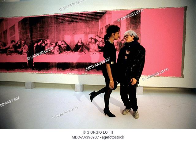 Andy Warhol watching a model. American artist Andy Warhol (Andrew Warhola Jr.) watching a model in front of the painting The Last Supper. Milan, 1986