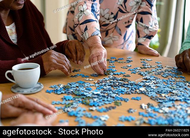 Hands of two diverse senior women and african american male friend doing puzzles. socializing with friends at home. || Model approval available