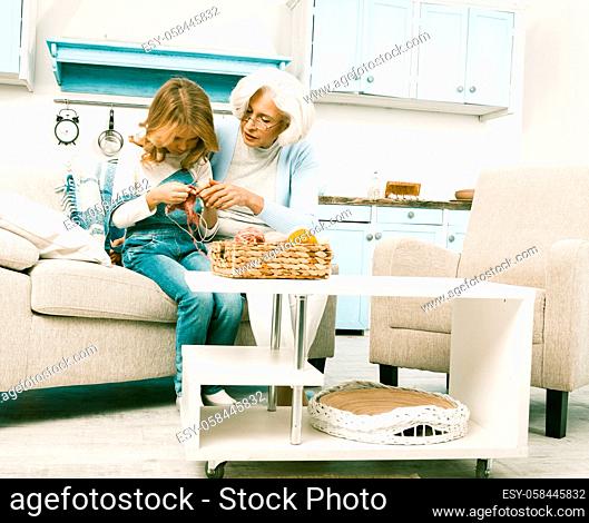 Family reunion white haired grandmother and her beloved granddaughter in jeans overall knitting socks or winter hats for whole family while staying at home