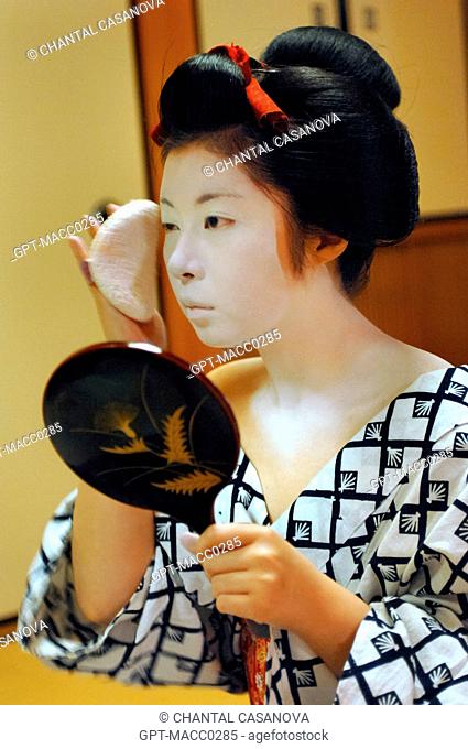 A MAIKO APPRENTICE GEISHA WITH HER TRADITIONAL MAKEUP DORAN. APPLICATION OF RICE POWDER WITH A SPONGE KONYAKU ON HER FACE OVER THE WHITE FOUNDATION SHIRONURI