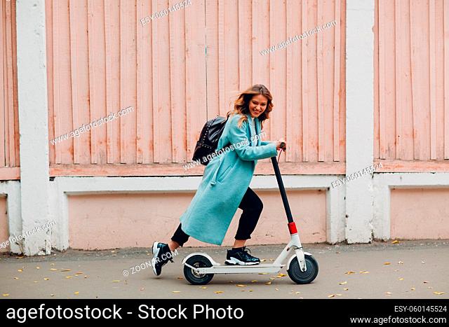 Young woman in coat ride electric scooter at the city in autumn weather