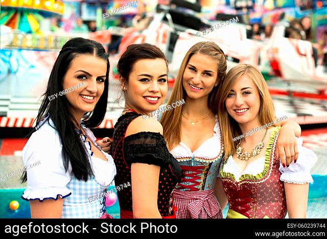 Joyful young and attractive women at German funfair Oktoberfest with traditional dirndl dresses and joyride in the background