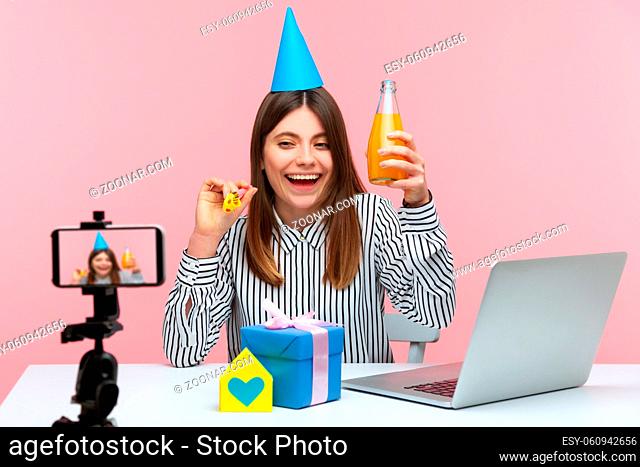 Cheerful optimistic woman blogger celebrating birthday with subscribers, posing at smartphone camera, recording video, online streaming