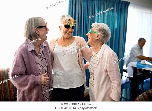 Senior female friends wearing novelty glasses talking at nursing home