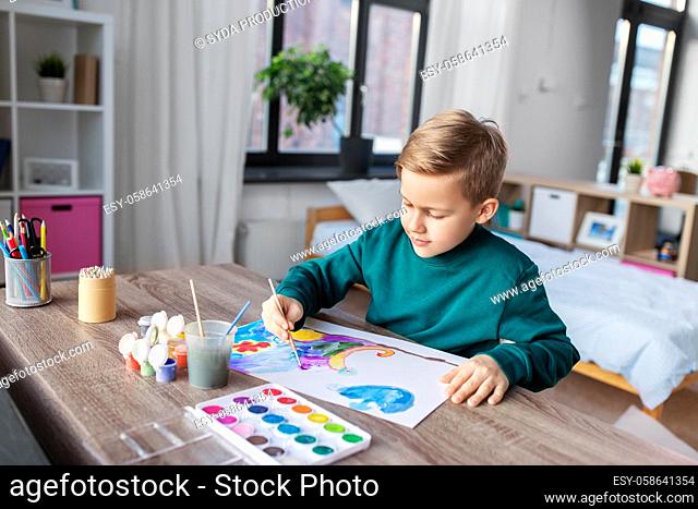 boy with colors and brush drawing picture at home