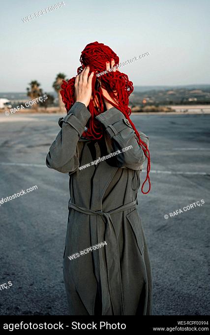 Woman covering face with thread standing on road