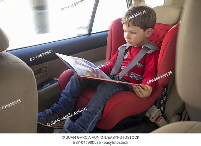 Toddler boy reading book in child car seat. Entertainment in the car for children concept