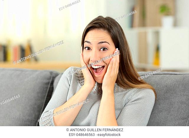 Surprised lady looking at you sitting on a couch in the living room at home