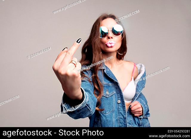 Offensive gesture showing at camera. Stylish young brunette in mirrored sunglasses showing middle finger with black nail