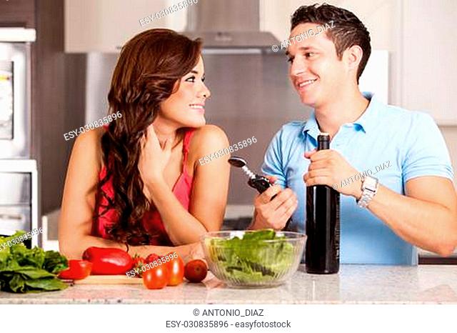 Happy brunette and her boyfriend cooking dinner and about to open a bottle of wine