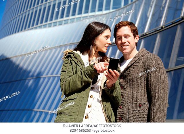 Young couple looking at mobile phone in the city, smartphone, Iberdrola Tower, Abandoibarra, Bilbao, Bizkaia, Basque Country, Spain