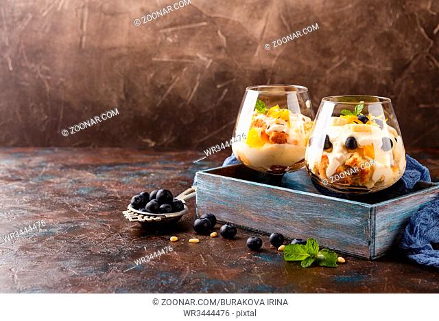 Healthy homemade layered dessert trifle with orange, blueberry, biscuit, yogurt and granola in a glasses in wooden box. Place for text
