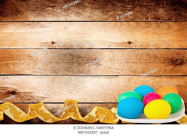 Wooden background with multicolored eggs in a bowl to celebrate Easter